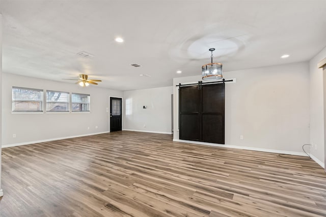 unfurnished living room with light hardwood / wood-style flooring, a barn door, and ceiling fan