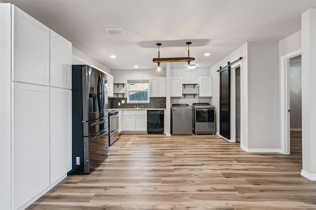 kitchen with appliances with stainless steel finishes, white cabinets, washing machine and clothes dryer, decorative light fixtures, and a barn door