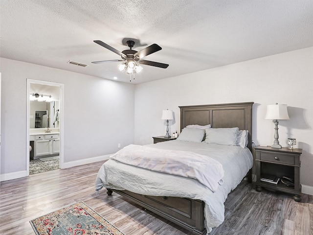 bedroom with a textured ceiling, connected bathroom, hardwood / wood-style flooring, and ceiling fan