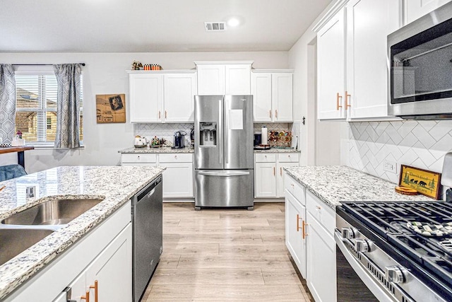 kitchen featuring light stone counters, white cabinetry, backsplash, and appliances with stainless steel finishes