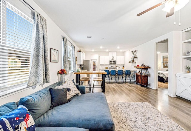 living room with built in shelves, light hardwood / wood-style floors, and ceiling fan