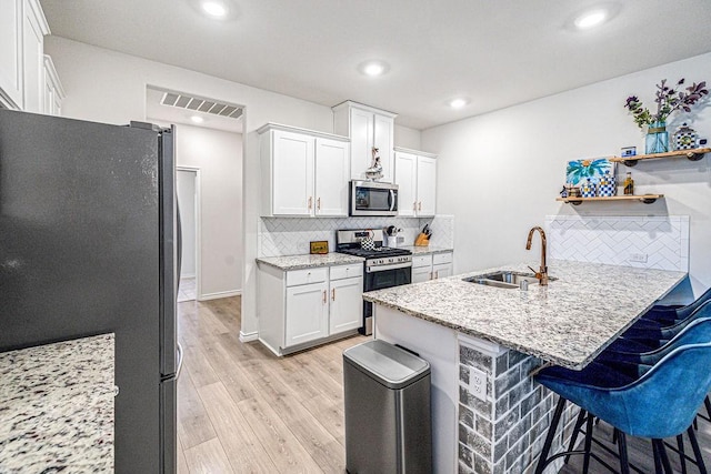 kitchen with a breakfast bar, sink, decorative backsplash, appliances with stainless steel finishes, and white cabinetry