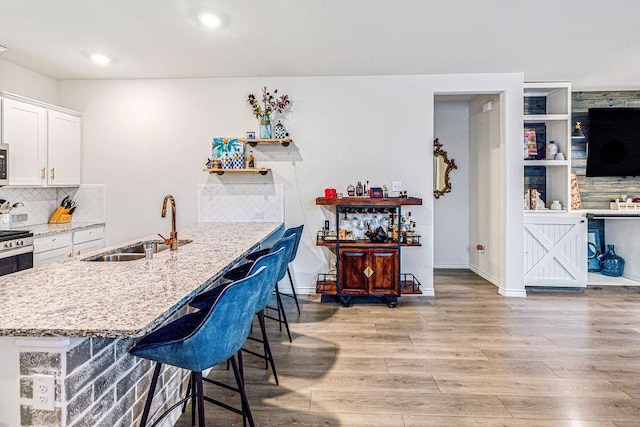 kitchen featuring sink, light stone counters, a breakfast bar area, white cabinets, and light wood-type flooring