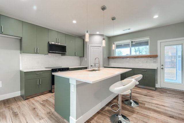 kitchen featuring sink, green cabinets, decorative light fixtures, a kitchen bar, and appliances with stainless steel finishes