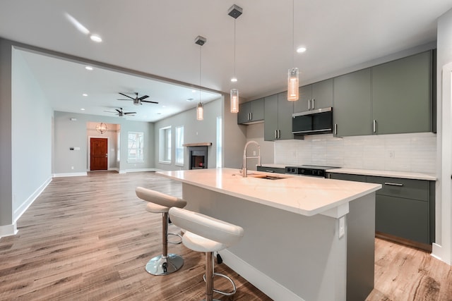 kitchen featuring appliances with stainless steel finishes, backsplash, light stone counters, decorative light fixtures, and an island with sink