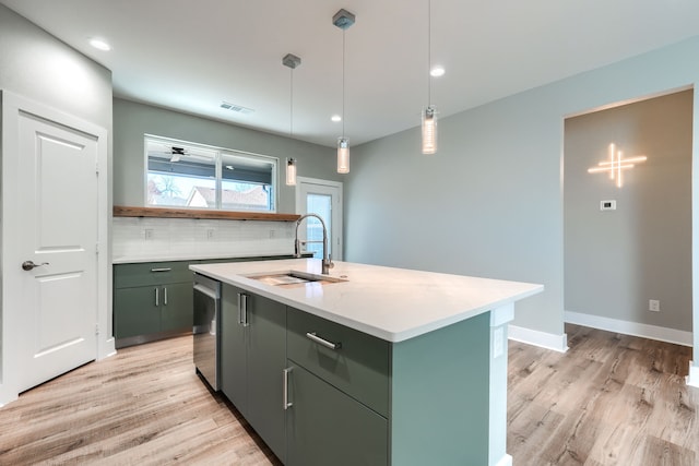 kitchen featuring backsplash, stainless steel dishwasher, a kitchen island with sink, sink, and decorative light fixtures