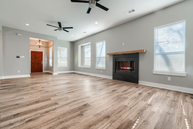 unfurnished living room featuring ceiling fan with notable chandelier and light wood-type flooring