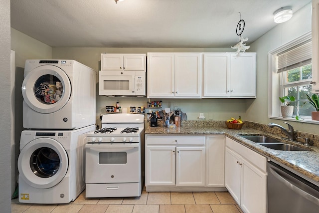 kitchen with white appliances, stacked washing maching and dryer, white cabinetry, and sink