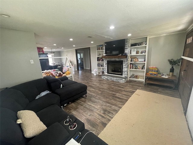 living room featuring crown molding, built in features, dark hardwood / wood-style floors, a textured ceiling, and a stone fireplace