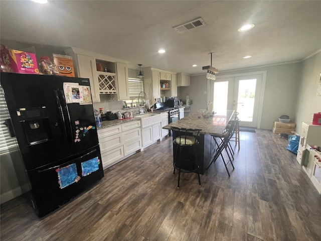 kitchen featuring a breakfast bar area, light stone countertops, a kitchen island, black fridge with ice dispenser, and decorative light fixtures