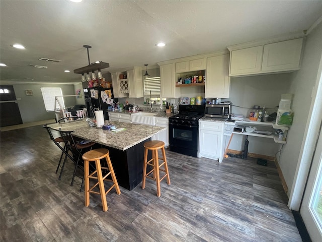 kitchen featuring black gas range oven, hanging light fixtures, a kitchen breakfast bar, a center island, and light stone counters