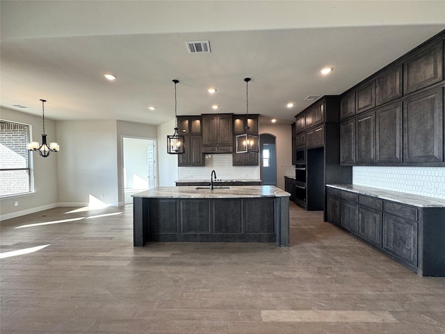 kitchen with hardwood / wood-style floors, backsplash, sink, an island with sink, and decorative light fixtures