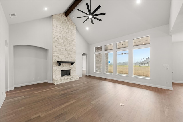 unfurnished living room with beam ceiling, wood-type flooring, a stone fireplace, and ceiling fan