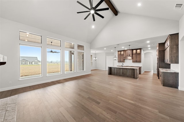 unfurnished living room featuring sink, beamed ceiling, light hardwood / wood-style floors, and ceiling fan