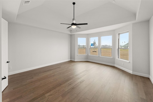 unfurnished room with a tray ceiling, dark wood-type flooring, and ceiling fan