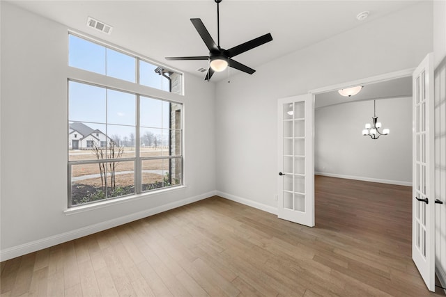 empty room featuring ceiling fan with notable chandelier, hardwood / wood-style floors, and french doors