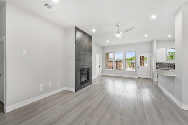 unfurnished living room featuring ceiling fan, light wood-type flooring, and a tile fireplace