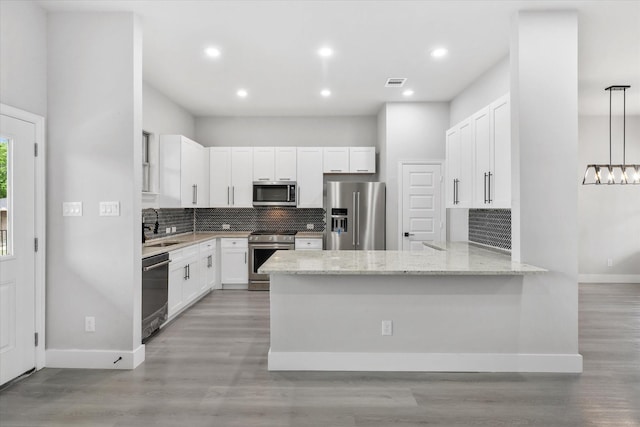 kitchen with light stone countertops, white cabinetry, hanging light fixtures, kitchen peninsula, and appliances with stainless steel finishes