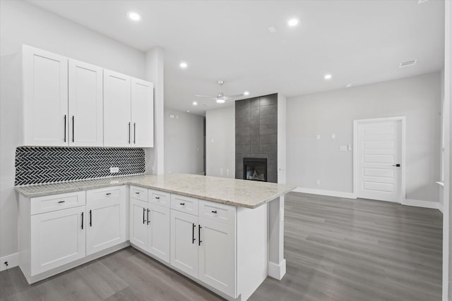 kitchen featuring light stone countertops, kitchen peninsula, light hardwood / wood-style floors, a fireplace, and white cabinets