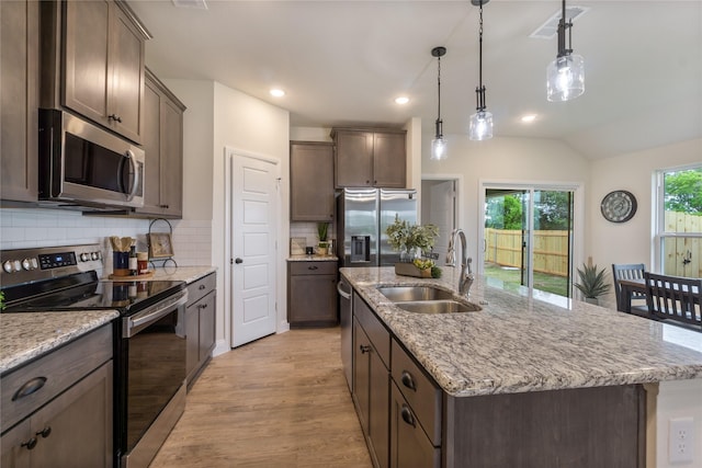 kitchen with a center island with sink, sink, hanging light fixtures, light wood-type flooring, and stainless steel appliances