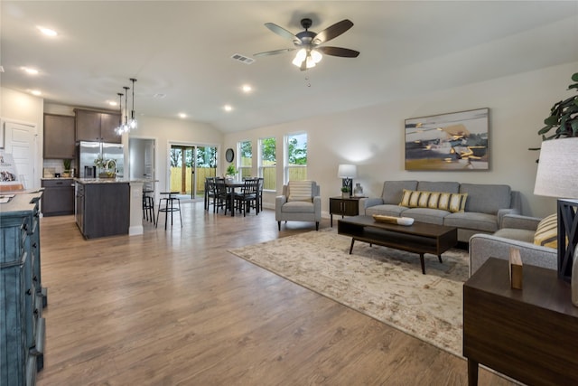 living room with ceiling fan, light hardwood / wood-style flooring, and vaulted ceiling