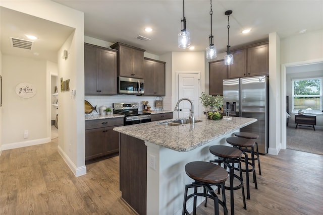 kitchen featuring sink, light stone counters, a breakfast bar, a center island with sink, and appliances with stainless steel finishes