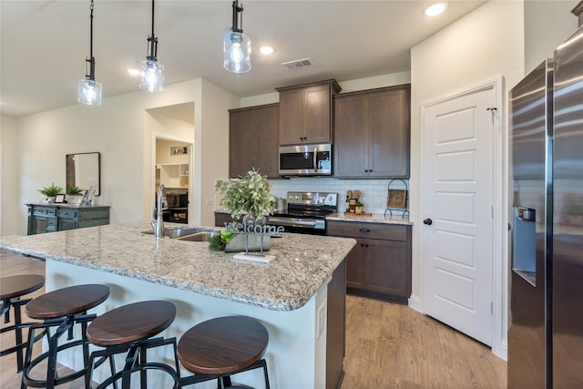 kitchen featuring stainless steel appliances, light stone counters, hanging light fixtures, and a center island with sink