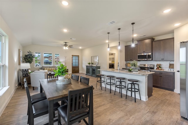 dining room featuring ceiling fan, sink, vaulted ceiling, and light wood-type flooring