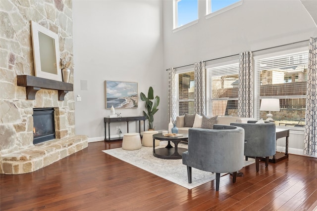 living room with a towering ceiling, dark hardwood / wood-style floors, and a stone fireplace