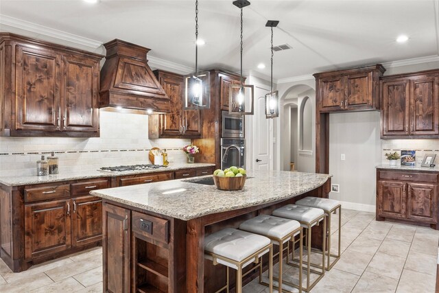 kitchen featuring stainless steel appliances, light stone counters, pendant lighting, a center island with sink, and custom exhaust hood