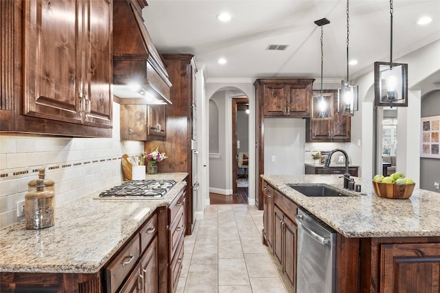 kitchen featuring appliances with stainless steel finishes, light stone counters, sink, decorative light fixtures, and an island with sink