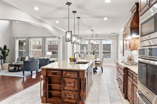 kitchen featuring light stone countertops, sink, decorative light fixtures, a kitchen island with sink, and appliances with stainless steel finishes