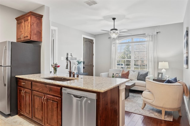 kitchen with sink, ceiling fan, appliances with stainless steel finishes, light hardwood / wood-style floors, and light stone counters