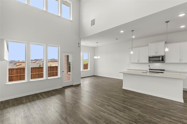 unfurnished living room featuring a notable chandelier, a towering ceiling, sink, and dark wood-type flooring