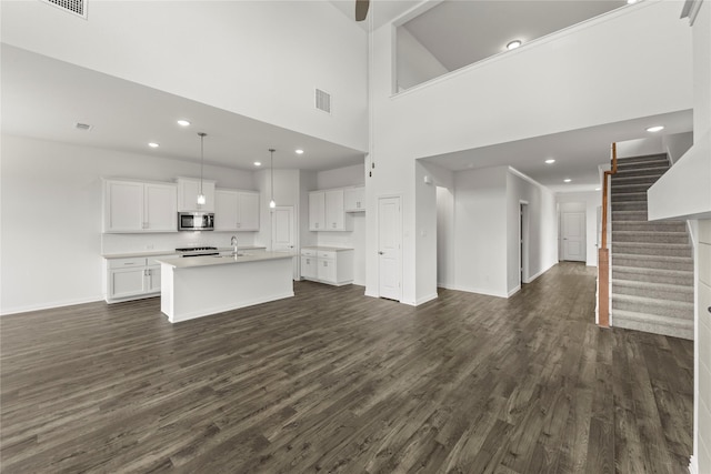 unfurnished living room with sink, a towering ceiling, and dark wood-type flooring