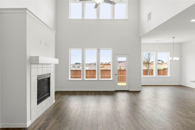 unfurnished living room featuring a fireplace, a high ceiling, ceiling fan with notable chandelier, and dark wood-type flooring