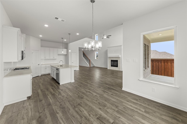 kitchen with a kitchen island with sink, ceiling fan, decorative light fixtures, white cabinetry, and a tiled fireplace