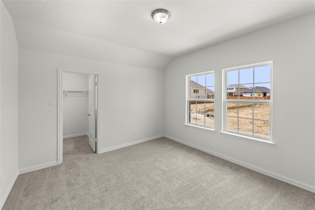 unfurnished bedroom featuring a walk in closet, light colored carpet, a closet, and lofted ceiling