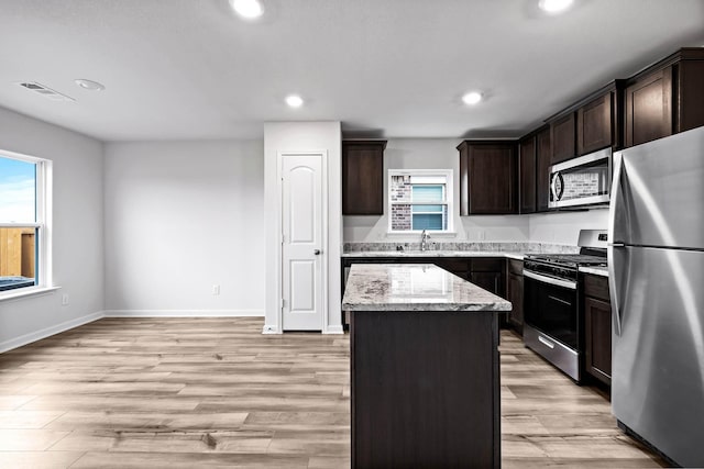 kitchen with light stone countertops, light wood-type flooring, dark brown cabinets, stainless steel appliances, and a kitchen island