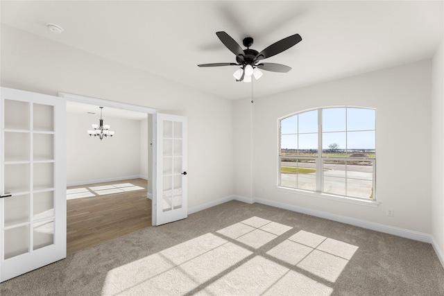 spare room featuring french doors, carpet flooring, and ceiling fan with notable chandelier