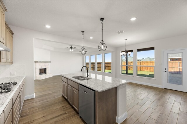 kitchen with dark wood-type flooring, light stone counters, backsplash, decorative light fixtures, and a center island with sink