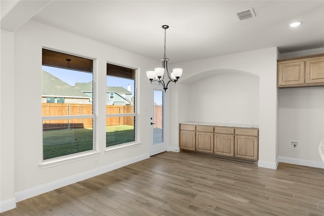 unfurnished dining area with plenty of natural light, hardwood / wood-style floors, and a notable chandelier