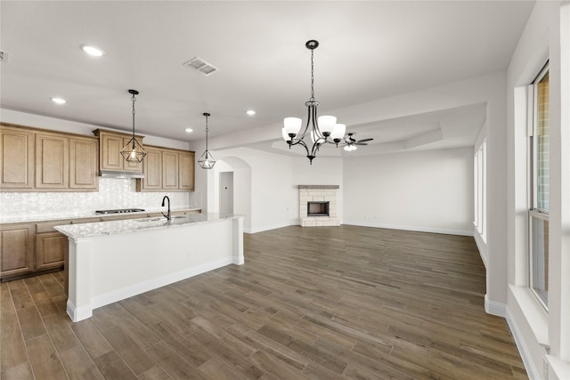 kitchen featuring a kitchen island with sink, hanging light fixtures, dark hardwood / wood-style floors, light stone counters, and decorative backsplash