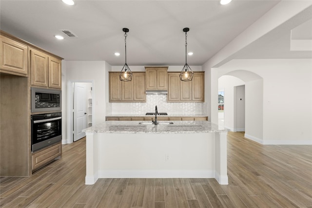 kitchen featuring built in microwave, light stone countertops, stainless steel oven, and a center island with sink