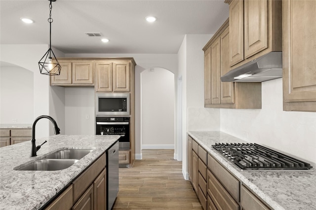 kitchen featuring sink, light stone counters, decorative light fixtures, appliances with stainless steel finishes, and hardwood / wood-style flooring