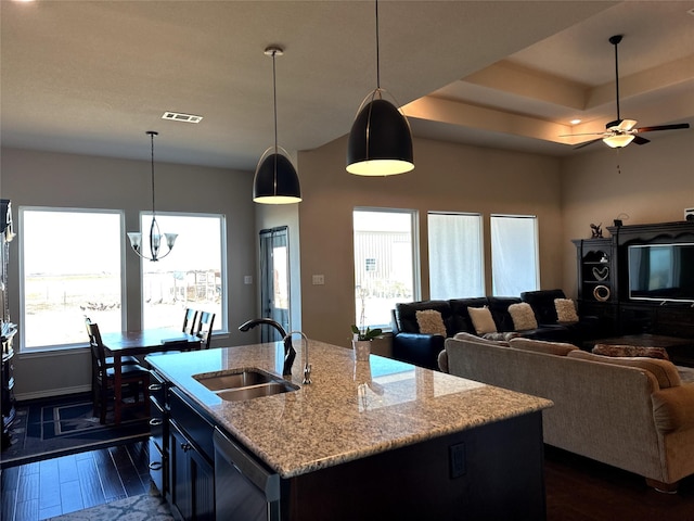 kitchen with pendant lighting, sink, light stone counters, dark wood-type flooring, and a center island with sink