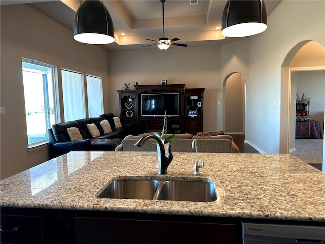 kitchen with light stone counters, sink, dishwasher, and a kitchen island with sink