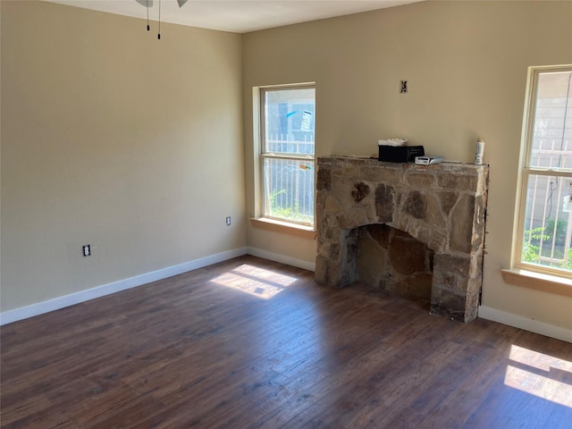 unfurnished living room with a healthy amount of sunlight, baseboards, dark wood-style flooring, and a stone fireplace