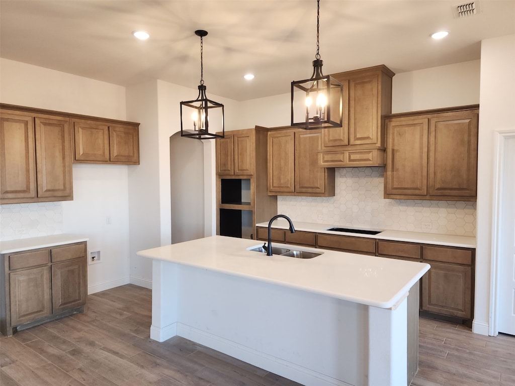 kitchen featuring pendant lighting, a kitchen island with sink, black electric stovetop, sink, and hardwood / wood-style flooring