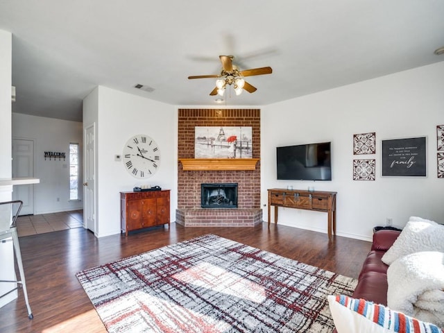 living room featuring dark hardwood / wood-style floors, a brick fireplace, and ceiling fan